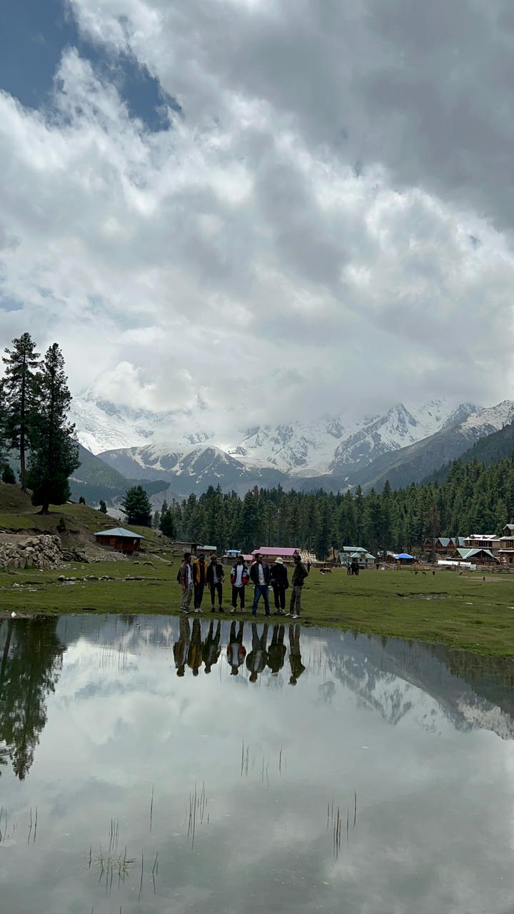 Group of trekkers reflected in a still alpine lake with snow peaks behind