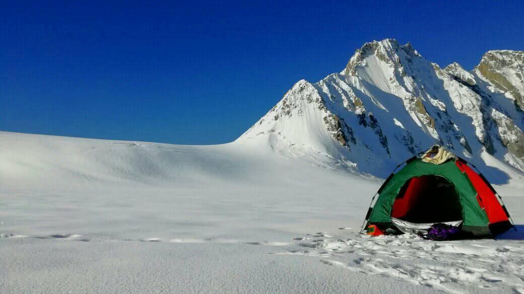 Dome tent pitched on a snowfield beneath jagged glacier peaks